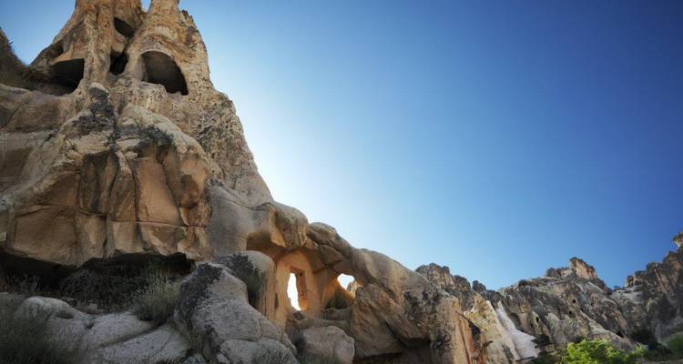 Acantilados rocosos erosionados dramáticos y cuevas bajo un cielo azul profundo en un paisaje semiárido.