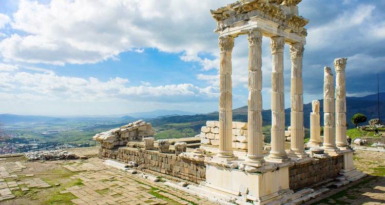 Restos de altas columnas de mármol blanco de un antiguo templo en la cima de una colina con vista a un extenso paisaje rural bajo cielos parcialmente nublados.