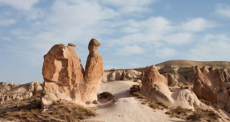Formaciones rocosas rojizas distintivas y chimeneas de hadas que se elevan desde un valle arenoso bajo un cielo ligeramente nublado.