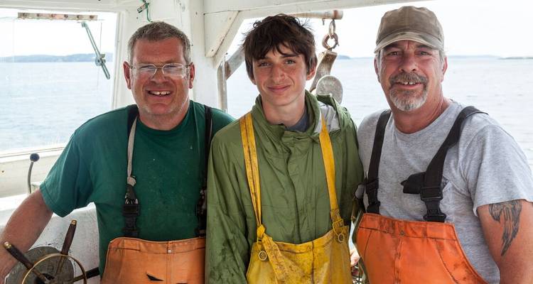 Three fishermen posing on a boat with fishing gear