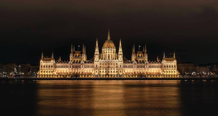 El Parlamento Húngaro brilla con luces doradas por la noche, reflejándose perfectamente en el río Danubio.