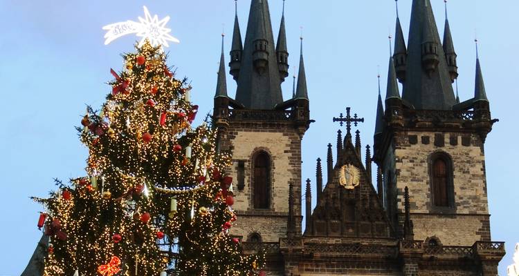 Un sapin de Noël imposant et décoré se dresse devant l'église gothique de la Tyn à Prague au crépuscule.
