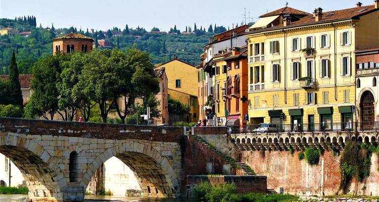 Kleurrijke gebouwen aan de rivier en een oude stenen brug in Verona onder de felle zon.