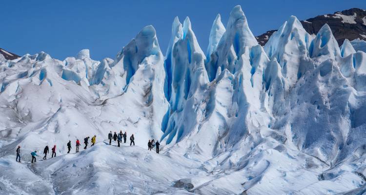 Group of people walking on a vast glacier under clear blue skies.
