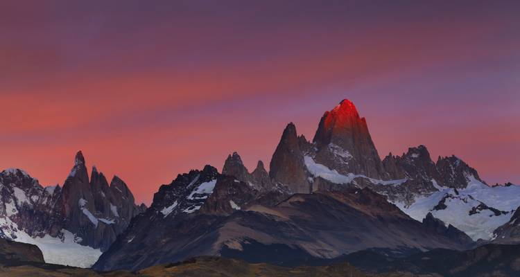 Mountain range with a red-lit peak during sunset.