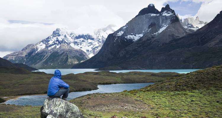 A person sitting on a rock overlooking a lake with majestic mountains.