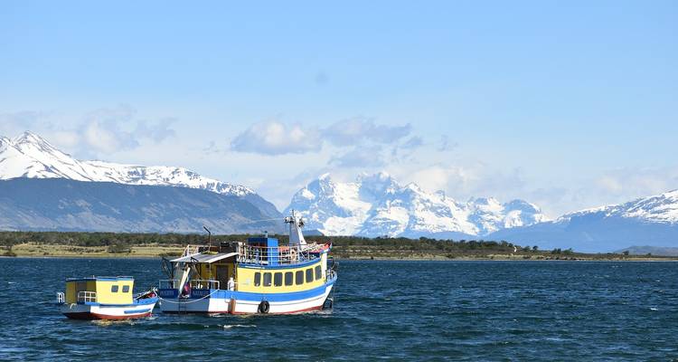 A boat navigating a lake with snow-covered mountains in the background.