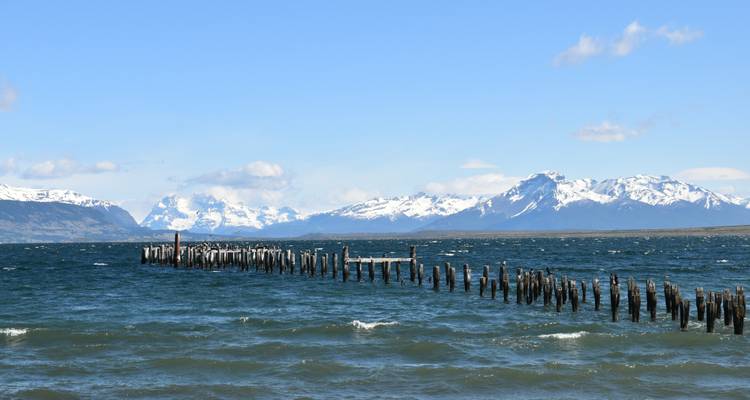 A scenic view of a lake with remnants of old pier posts and mountains.
