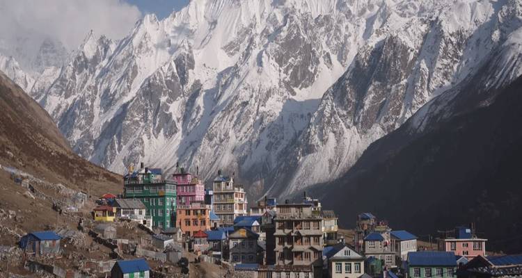 Pueblo himalayo con techos coloridos acurrucado bajo montañas nevadas que se alzan imponentes.
