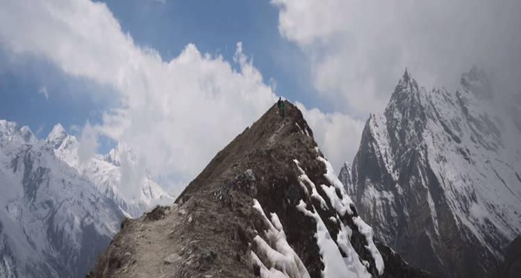 Un excursionista solitario sube por una cresta nevada hacia los picos escarpados del Himalaya bajo nubes dramáticas.
