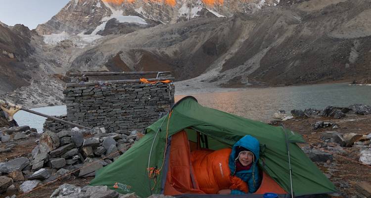 Camper an einem See nahe einem Gebirgszug unter blauem Himmel.
