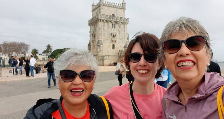Tres mujeres sonriendo frente a la Torre de Belém.