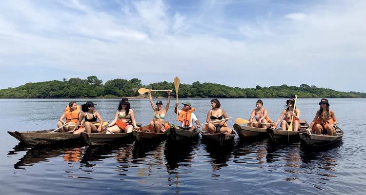 Groupe de voyageurs pagayant dans de petits canoës en bois sur une rivière calme de l'Amazonie.
