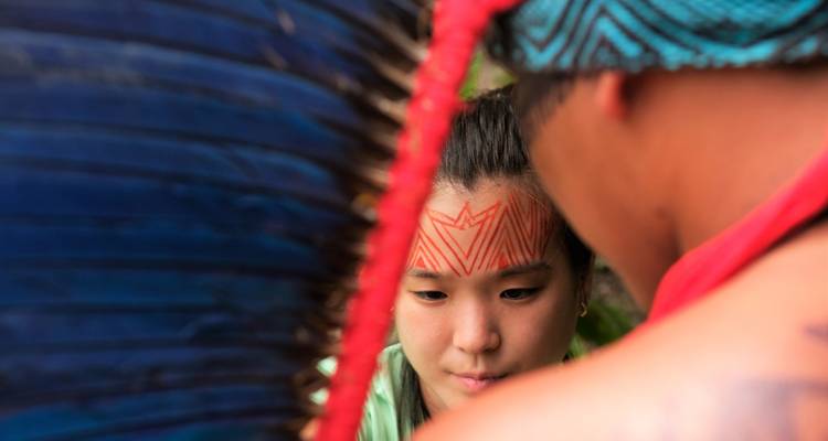 Gros plan d'un visiteur se faisant appliquer la peinture faciale rouge traditionnelle lors d'une rencontre culturelle autochtone.