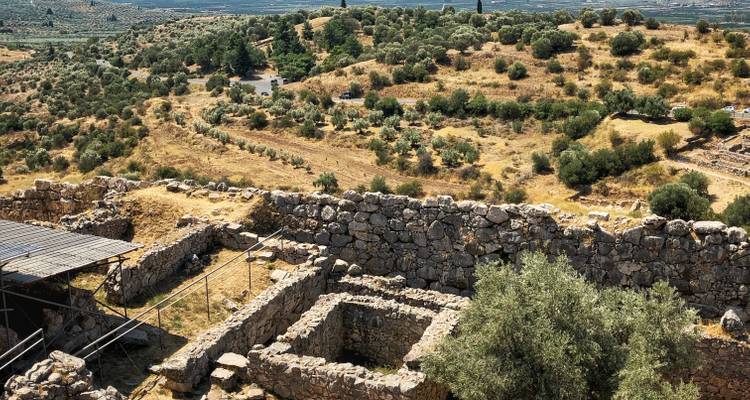 Antike Ruinen in einer trockenen Landschaft mit Olivenbäumen.