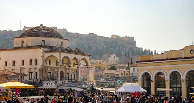 La bulliciosa Plaza Monastiraki llena de gente, puestos de mercado y una mezquita histórica con la Acrópolis arriba
