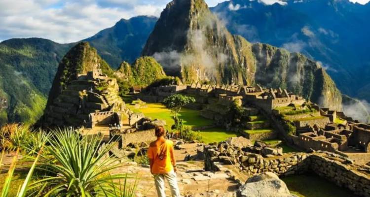 Iconic panoramic view of Machu Picchu ruins with a lone traveller in an orange shirt gazing over the site
