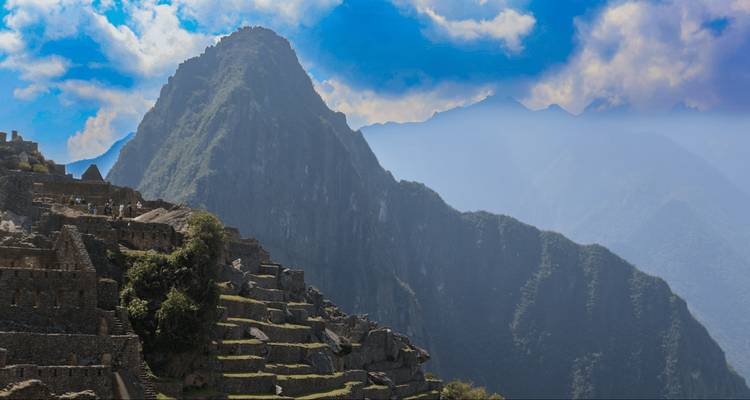 Side view of Machu Picchu terraces against steep green Andean cliffs in hazy afternoon light