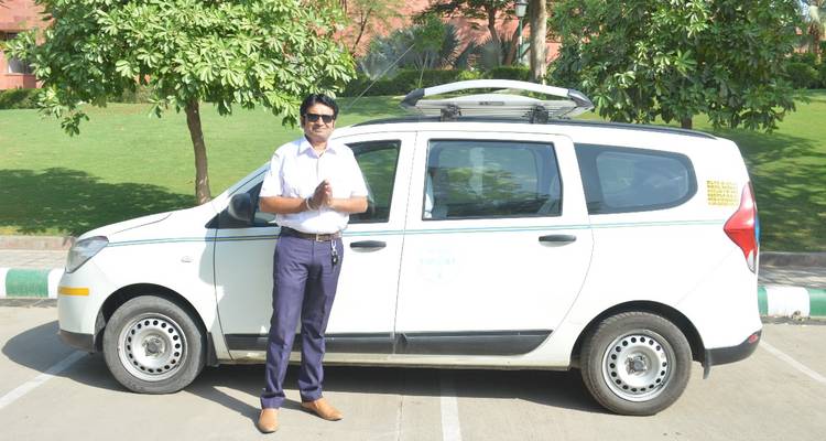 Un homme debout à côté d'une voiture blanche dans une zone de stationnement avec des pelouses vertes.