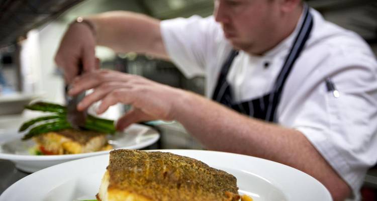 Chef dressant du poisson et des asperges dans une cuisine professionnelle