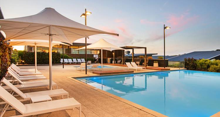 Piscine du resort bordée de chaises longues blanches et de voiles d'ombrage au crépuscule.