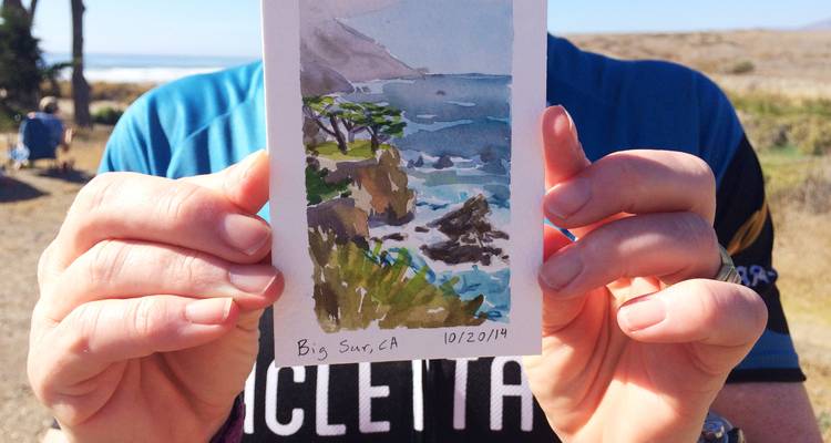 Person holding a watercolor of a coastal scene.