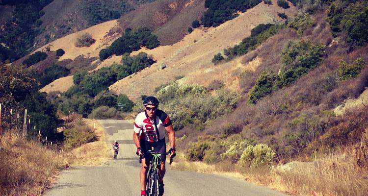 Cyclist on a hilly road surrounded by dry terrain.