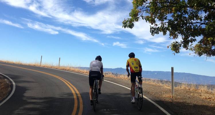 Two cyclists riding up a road under a blue sky.
