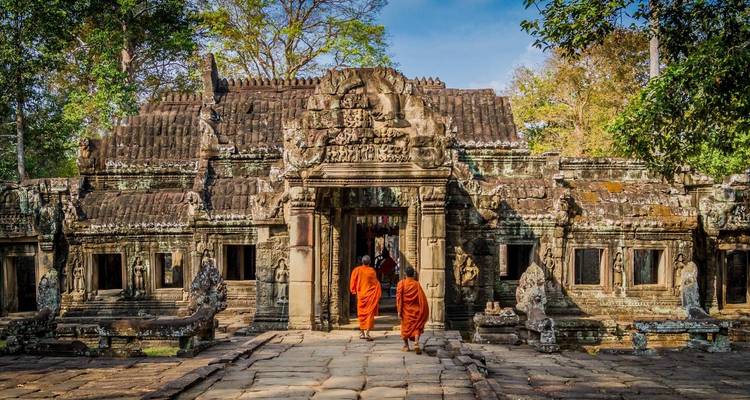 Monjes entrando a un templo de piedra decorado en un entorno forestal.