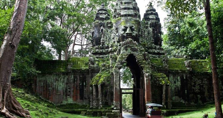 Una puerta de piedra histórica cubierta de musgo, con un tuk-tuk pasando.