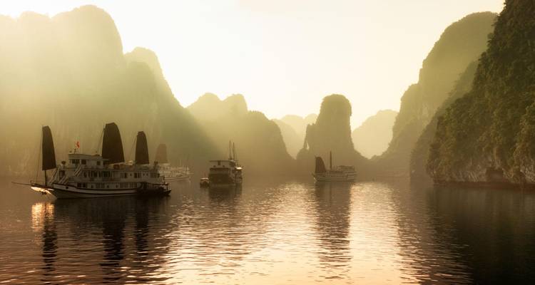La brumosa luz matutina envuelve los karsts de piedra caliza y los juncos de crucero en la Bahía de Ha Long.