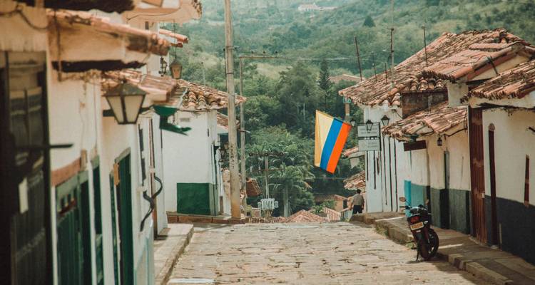 Calle empedrada con casas coloridas y una bandera colgando en un pueblo colonial.