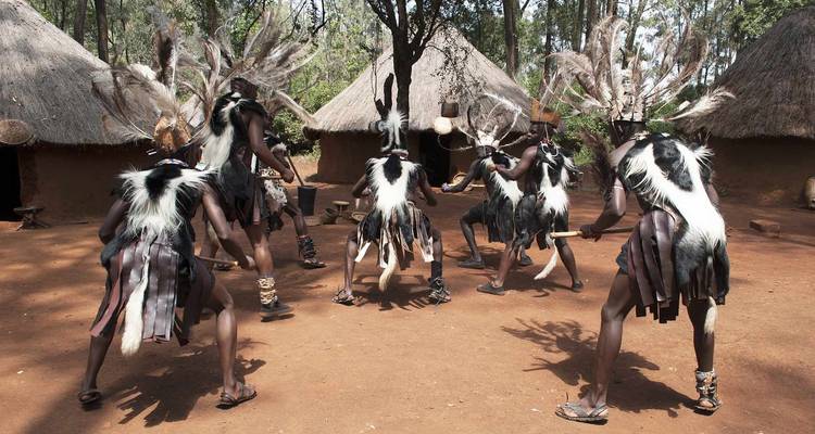 Group of traditional dancers performing outside huts.