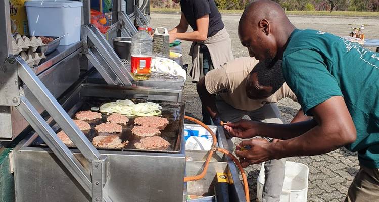 Des personnes faisant griller sur un barbecue avec des hamburgers prêts à cuire.