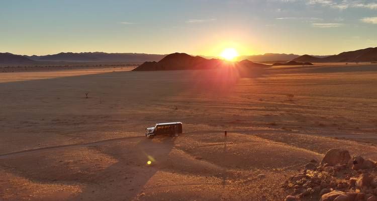 Atardecer sobre un vasto desierto con la silueta de un vehículo solitario.