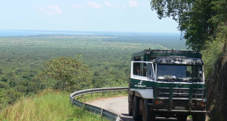 Safari truck on a winding road overlooking a vast landscape.