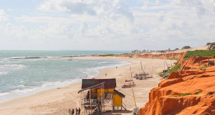 Belle plage avec des falaises rouges et de petites cabanes.
