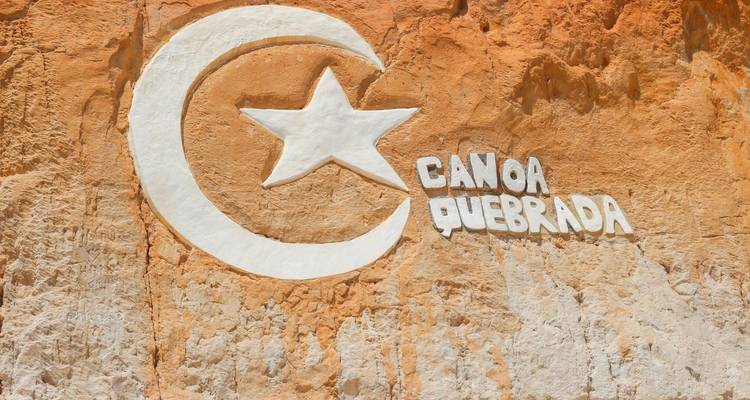 Symbole de Canoa Quebrada gravé sur un mur de roche rouge.