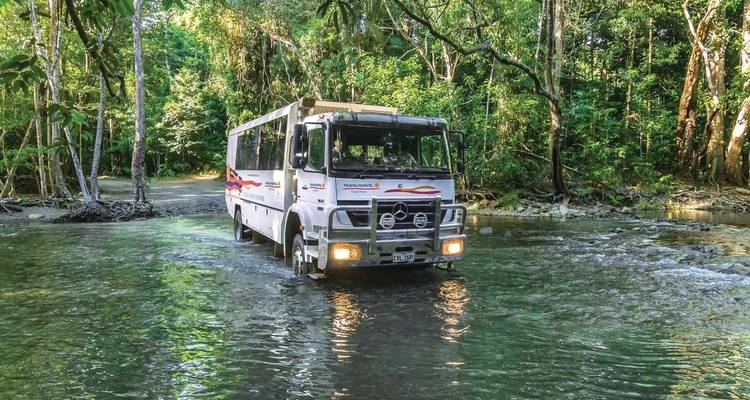 Ein Safari-Fahrzeug, das einen seichten Fluss in tropischer Umgebung durchquert.