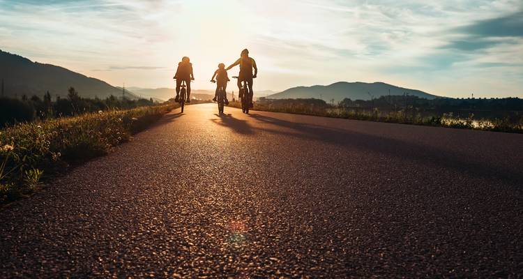 Silhouette of cyclists riding at sunset with mountains in the background.