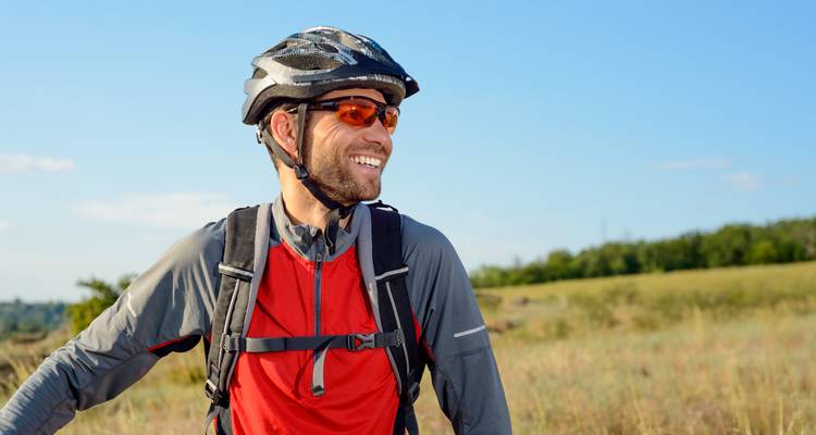 Portrait of a smiling man wearing a bicycle helmet in a field.
