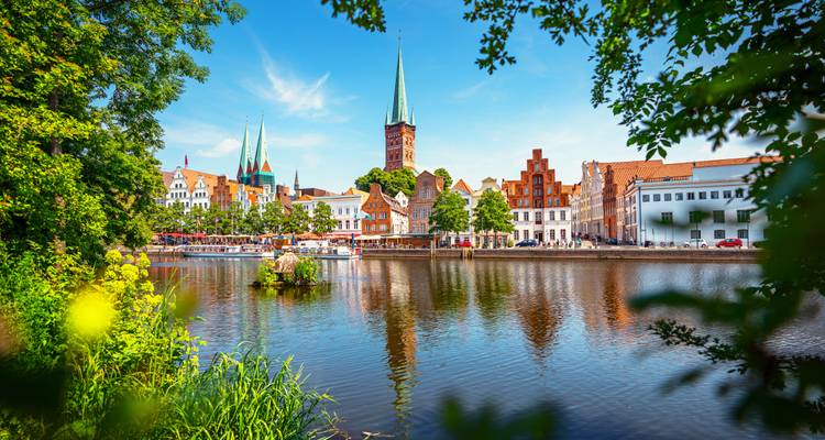 Een pittoresk stadje aan de rivier met historische gebouwen en hoge kerktorens omringd door weelderig groen.