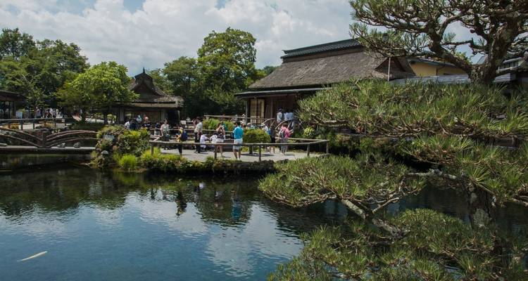 Une vue pittoresque d'un bâtiment traditionnel japonais près d'un étang avec des arbres et des gens qui profitent de la vue.