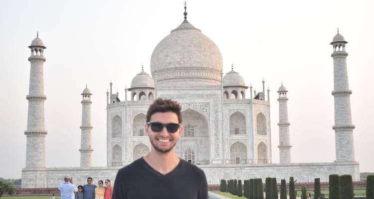 Smiling traveler posing in front of the Taj Mahal on a bright hazy day.