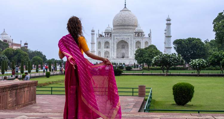 Woman in vibrant sari admiring the Taj Mahal from garden terrace.