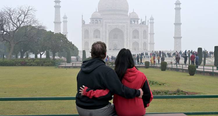 Couple seated arm in arm gazing at the fog-veiled Taj Mahal.