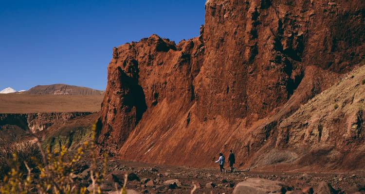 Wandelaars lopen naast torenhoge roestrodekleurige rotswanden in de Valley of Mars, Atacama.