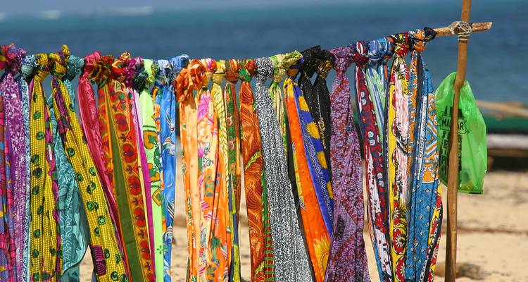 Une rangée colorée de foulards à motifs flottant sur un étal en bord de plage avec l'océan en arrière-plan.