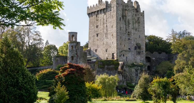 Le château de Blarney en pierre s'élève au-dessus de jardins soignés sous un ciel partiellement nuageux.