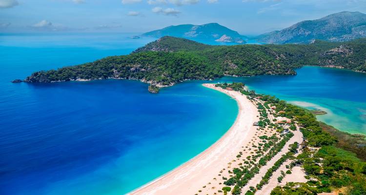 Vista aérea de la laguna turquesa de Ölüdeniz y las colinas verdes circundantes bajo el cielo azul.